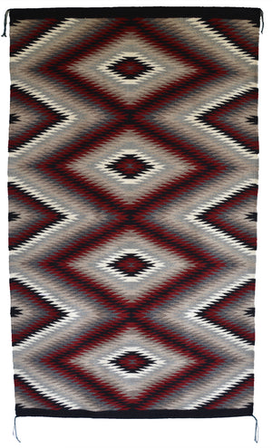 A Navajo eye dazzler rug with a Southwestern geometric diamond pattern in dark red, black, gray, beige, and white, shown flat against a white background.