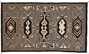 A Teec Nos Pos rectangular Navajo rug featuring Hero Twin designs, predominantly in brown tones with white and darker accents.