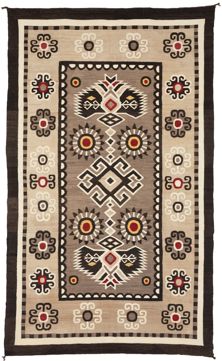 A vintage Bistie Navajo rug with geometric curvilinear designs, predominantly in brown, beige, and red, with a visible eagle tail design.