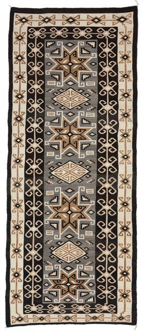 A rectangular Two Grey Hills Bistie Navajo rug featuring geometric patterns primarily in black, beige, and brown colors.